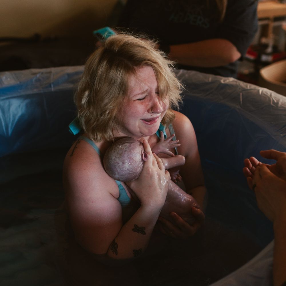 woman birthing baby in home birth tub